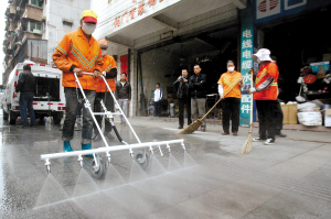 环卫工人使用路面养路车的洒水喷头清洁路面。