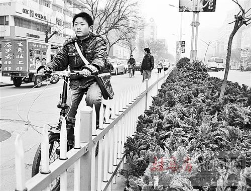 一孩子骑车从带箭头的护栏旁边经过。