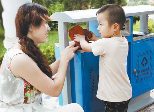 8月25日，庆城县一位年轻妈妈正在指导孩子向分类垃圾箱投放垃圾。