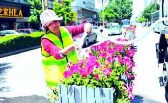 天水秦州工作员给民主路栏杆花箱内的鲜花浇水